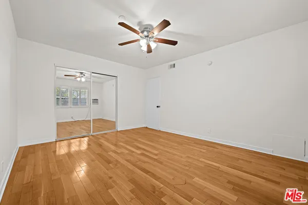 a view of an empty room with wooden floor and a ceiling fan