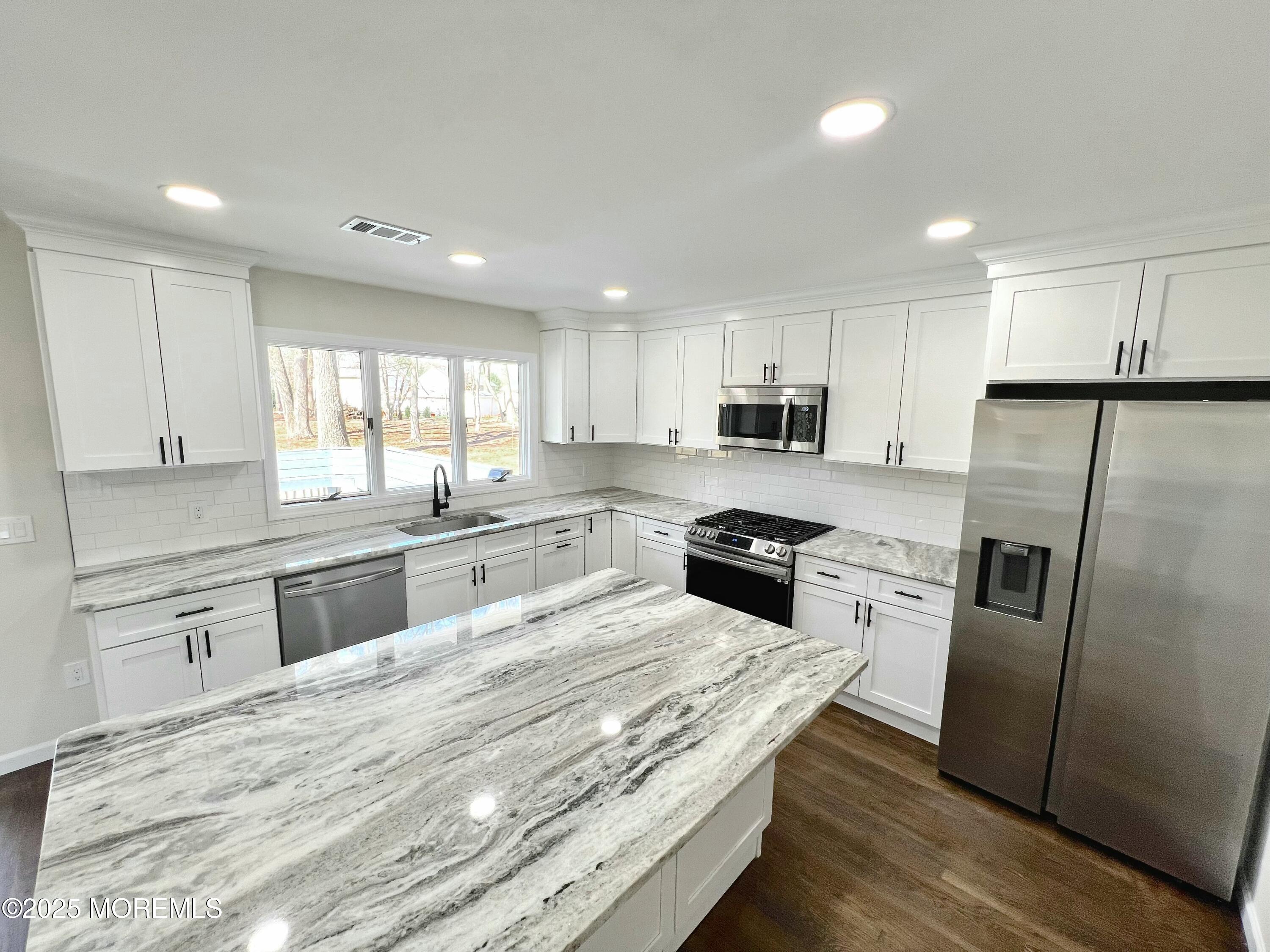 a large kitchen with granite countertop a large counter top stainless steel appliances and cabinets