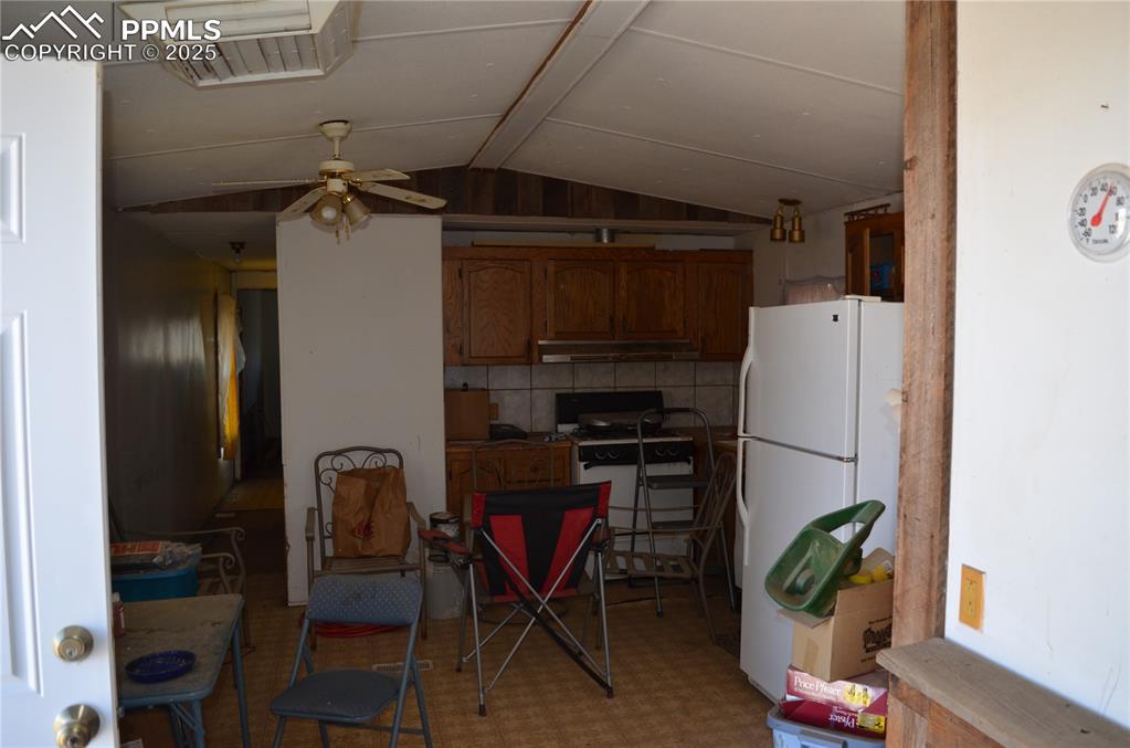 1604 County Road R Rush, CO 80833 - Photo 13 of 16 Kitchen with visible vents, under cabinet range hood, vaulted ceiling, white appliances, and brown cabinetry