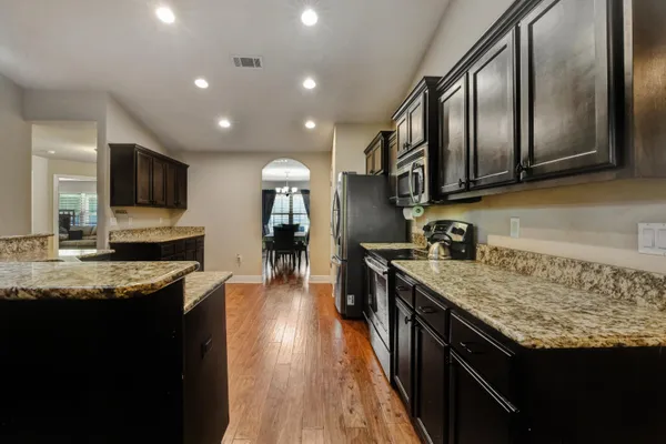 a large kitchen with stainless steel appliances granite countertop a stove a sink dishwasher and a microwave oven with wooden floor