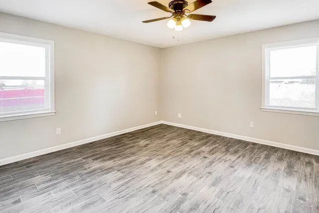 an empty room with wooden floor fan and windows