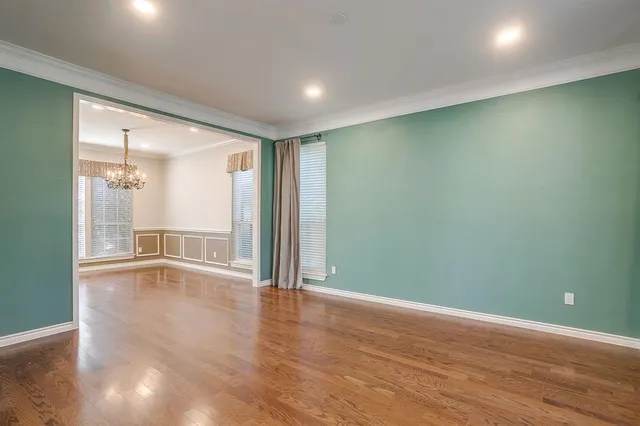 an empty room with wooden floor and windows with curtains