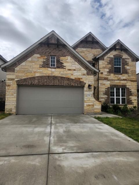 French provincial home with stone siding, driveway, and an attached garage