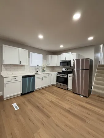 a large kitchen with stainless steel appliances granite countertop a stove a sink dishwasher a refrigerator and white cabinets with wooden floor