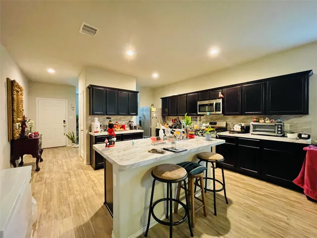 a kitchen with stainless steel appliances kitchen island granite countertop a sink dishwasher a stove and a refrigerator with wooden floor