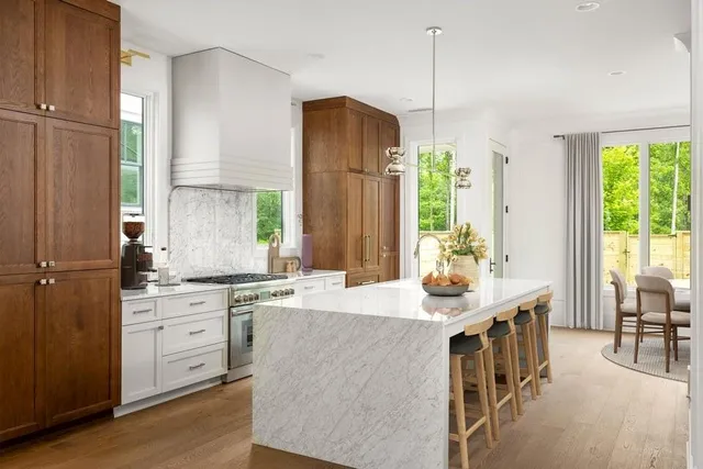 a kitchen with kitchen island granite countertop a stove a sink a dining table and chairs with wooden floor