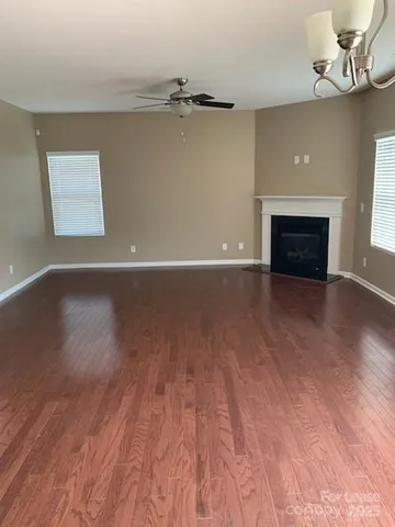 a view of an empty room with wooden floor fireplace and a window