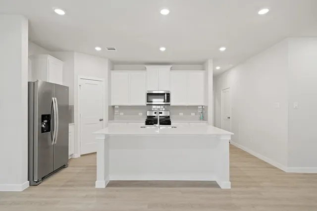 a large white kitchen with wooden floor and a refrigerator