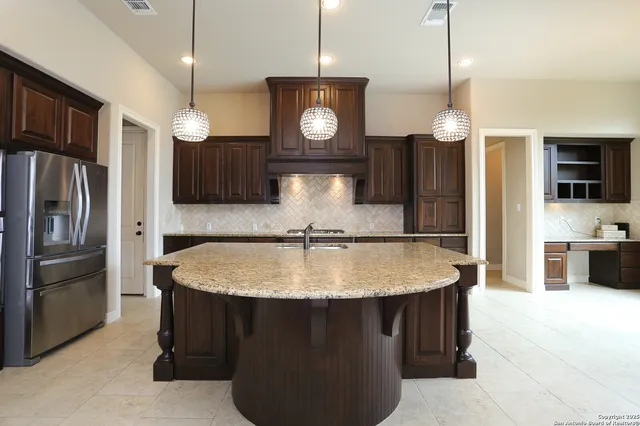 a kitchen with kitchen island granite countertop a sink a refrigerator and chairs