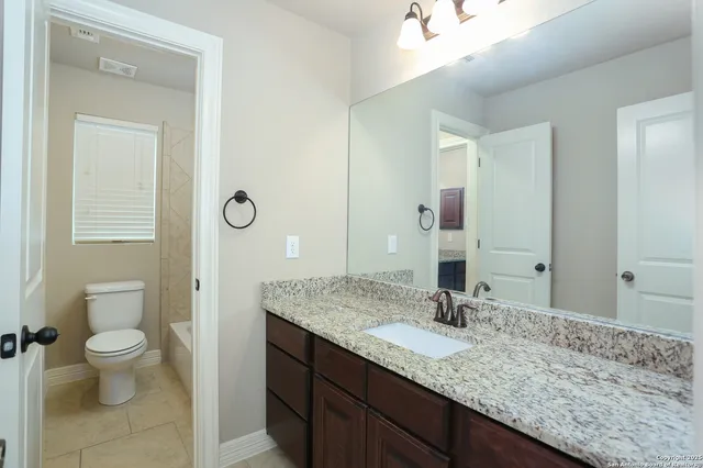 a bathroom with a granite countertop sink a toilet and a mirror
