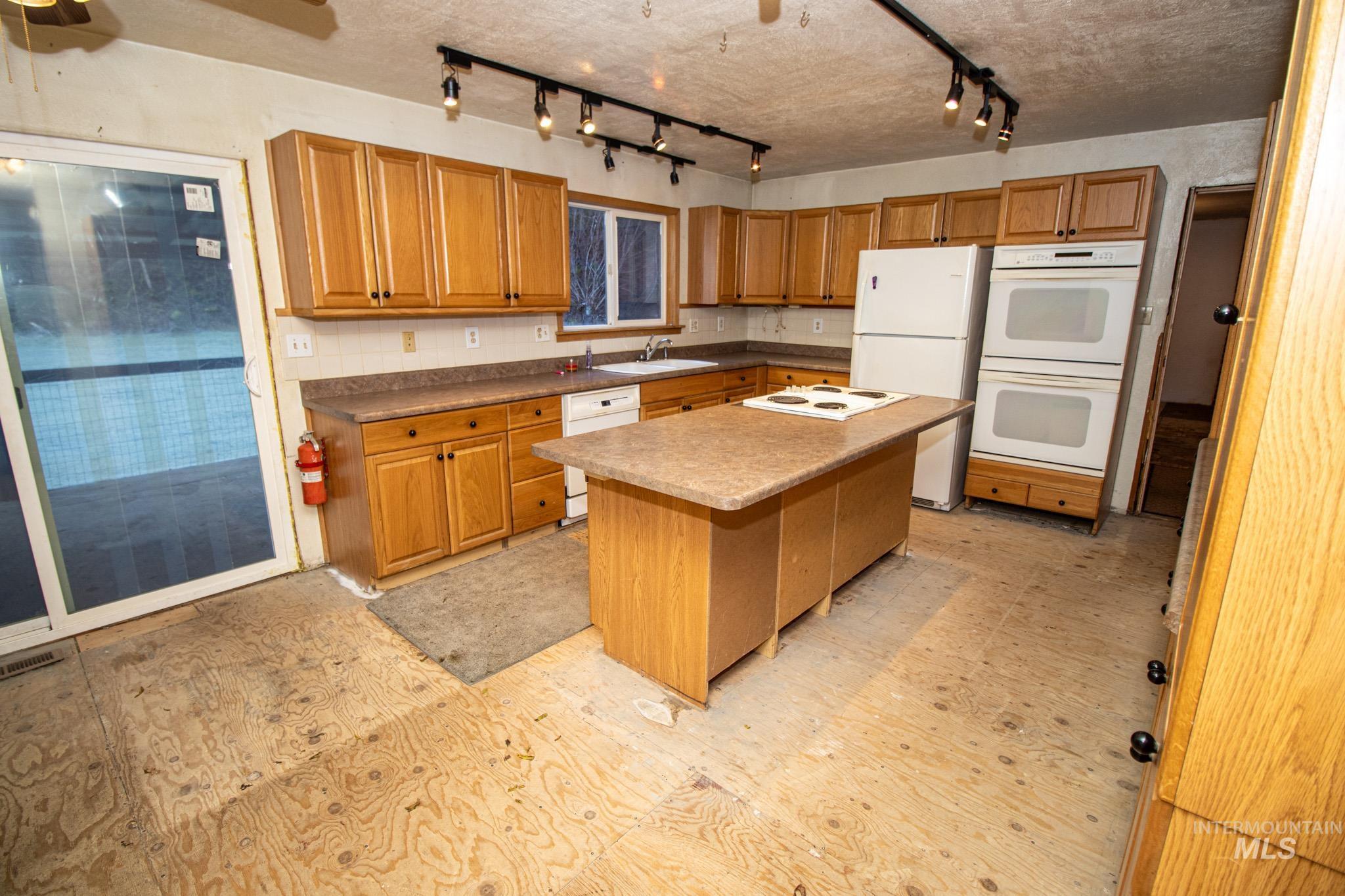404 Harmony Heights Road Orofino, ID 83544 - Photo 16 of 35 Kitchen with light flooring, white appliances, brown cabinetry, and a kitchen island