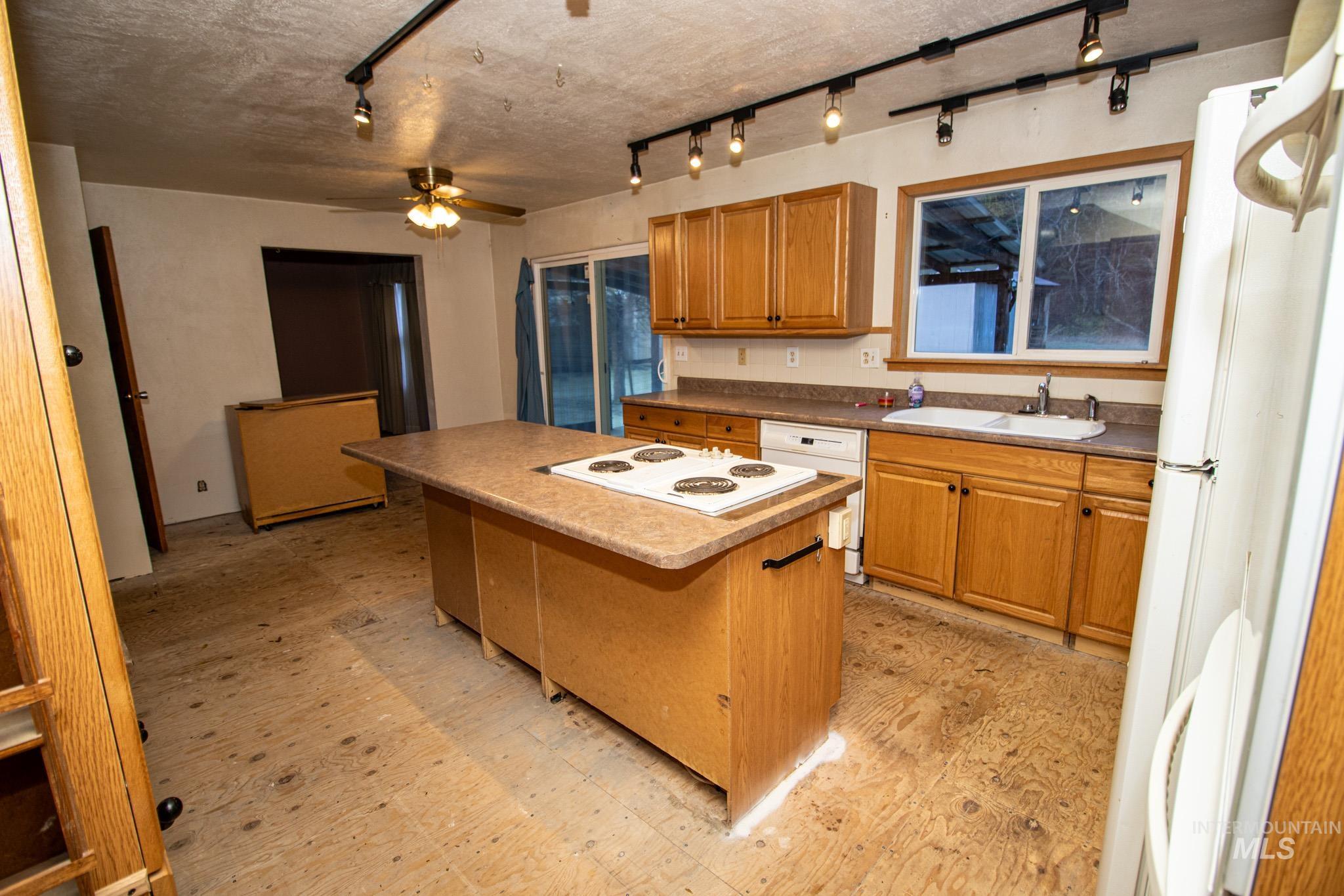 404 Harmony Heights Road Orofino, ID 83544 - Photo 17 of 35 Kitchen with a kitchen island, brown cabinetry, white appliances, light flooring, and a ceiling fan