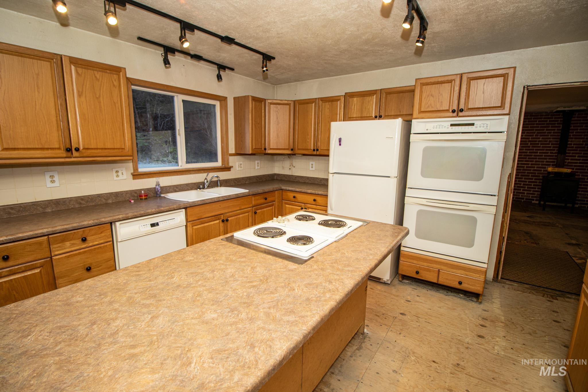 404 Harmony Heights Road Orofino, ID 83544 - Photo 18 of 35 Kitchen featuring white appliances, brown cabinetry, a textured ceiling, and track lighting