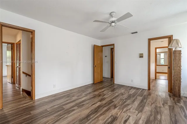 a view of an empty room with wooden floor and a ceiling fan