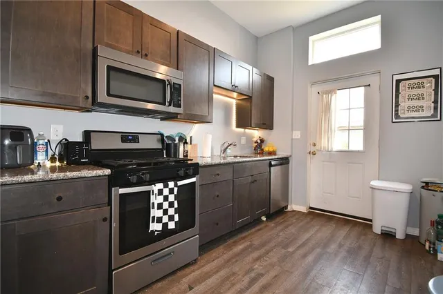 a kitchen with stainless steel appliances granite countertop wooden cabinets a refrigerator a sink a stove a microwave and wooden floors