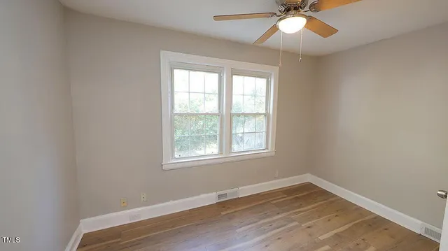 an empty room with wooden floor fan and windows