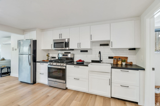 3813 North Foothill Drive Provo, UT 84604 - Photo 32 of 71 Modern kitchen featuring white shaker cabinetry, dark countertops, stainless steel appliances, a white subway tile backsplash with black accents, and wood-finish flooring