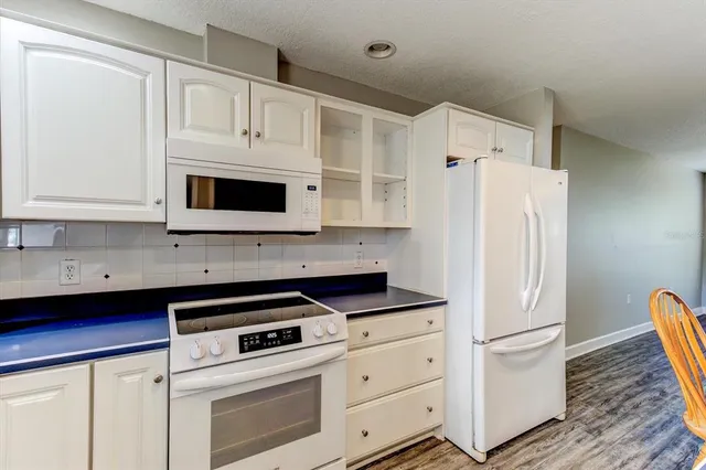 a kitchen with stainless steel appliances granite countertop a refrigerator a stove a sink and a dining table with wooden floor