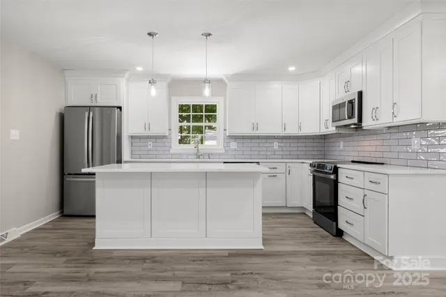 a kitchen with stainless steel appliances granite countertop a refrigerator a sink dishwasher a stove and white countertops with wooden floor