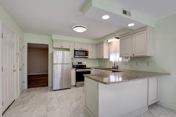 a kitchen with stainless steel appliances granite countertop a refrigerator a sink dishwasher a stove and white cabinets with wooden floor