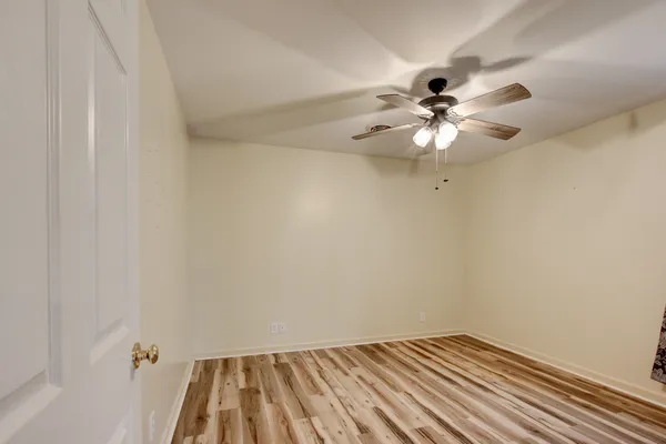 a view of an empty room with wooden floor and a ceiling fan
