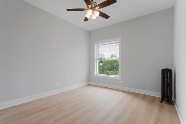 an empty room with wooden floor ceiling fan and window