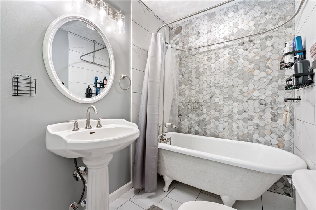 200 Echo Circle Easley, SC 29642 - Photo 16 of 35 A well-lit bathroom features a pedestal sink and a freestanding clawfoot tub, complemented by a honeycomb-tiled shower surround.