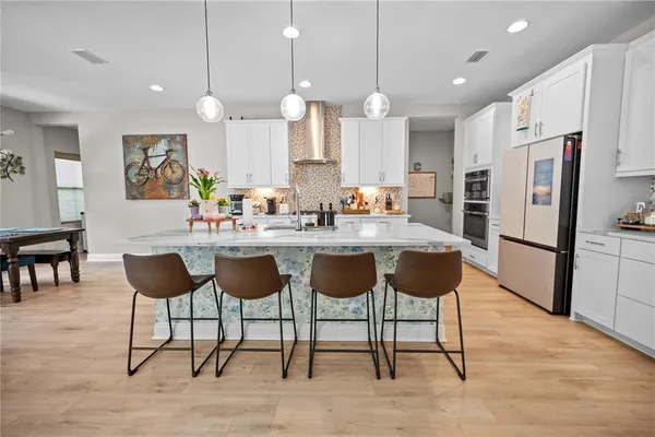 a kitchen with stainless steel appliances kitchen island granite countertop a dining table chairs and a refrigerator