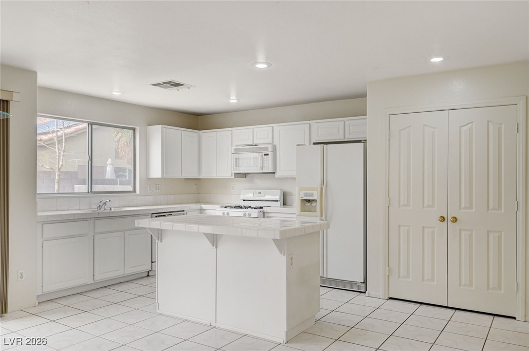 3901 Triora Street Las Vegas, NV 89129 - Photo 14 of 42 Kitchen featuring tile countertops, white appliances, white cabinetry, a kitchen island, and a breakfast bar area