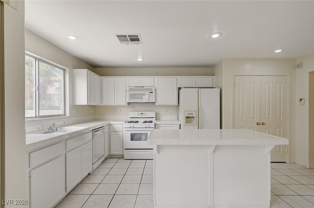 3901 Triora Street Las Vegas, NV 89129 - Photo 15 of 42 Kitchen featuring tile counters, white appliances, white cabinetry, a center island, and a breakfast bar area