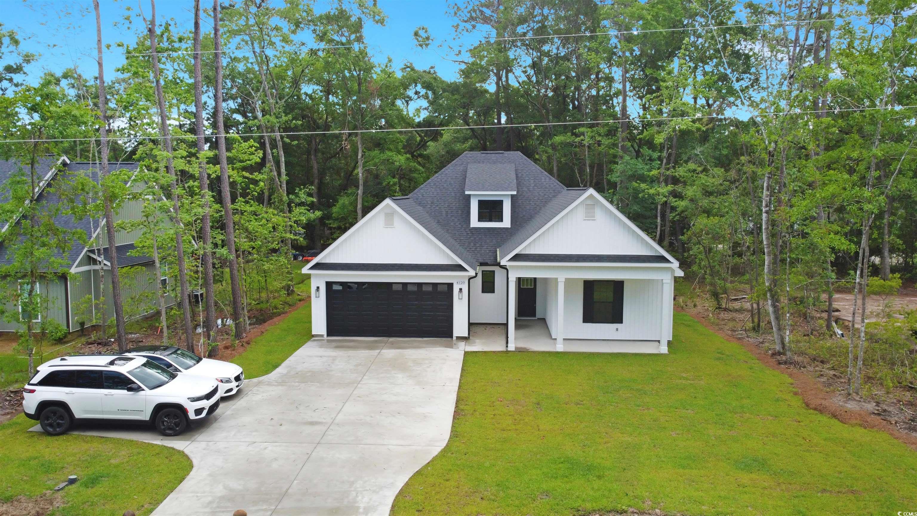 4121 Whatuthink Road Myrtle Beach, SC 29588 - Photo 4 of 28 Zoomed-out view of this traditional, farmhouse-inspired home featuring concrete driveway, and attached garage, a front yard, covered porch, and roof with shingles