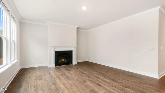 a view of an empty room with wooden floor fireplace and a window