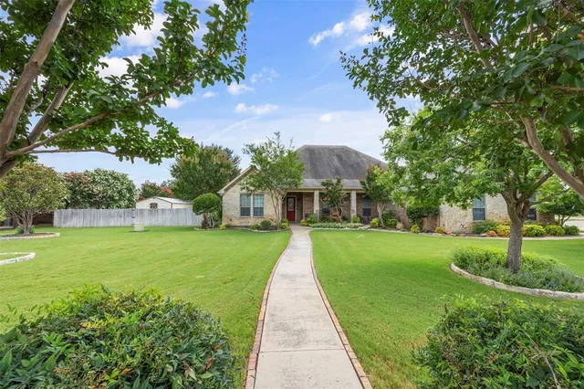 a view of a house with a big yard and potted plants and large trees