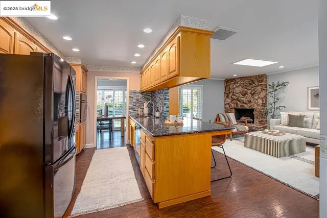 a kitchen with stainless steel appliances granite countertop a refrigerator a oven a sink and a dining table with wooden floor