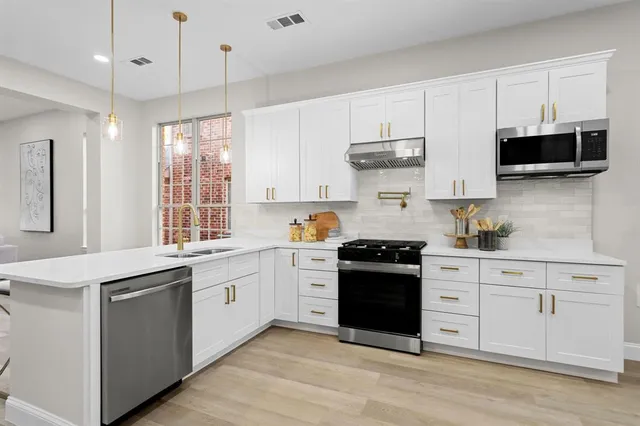 a large white kitchen with stainless steel appliances granite countertop a stove and a sink