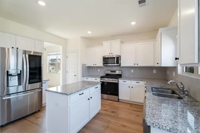 a kitchen with stainless steel appliances granite countertop a stove top oven a refrigerator a sink and dishwasher with wooden floor