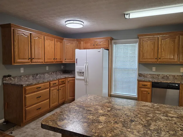 a kitchen with granite countertop a refrigerator stove top oven a sink and dishwasher