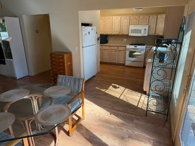 a kitchen with stainless steel appliances granite countertop a refrigerator a stove a sink a dining table and chairs with wooden floor