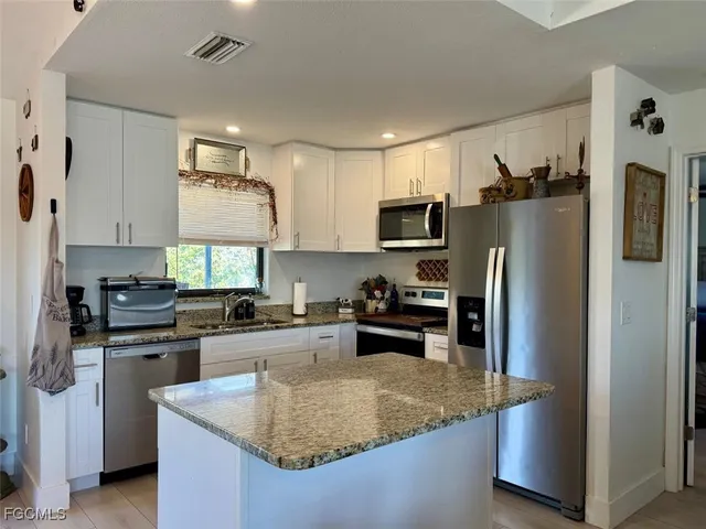 a kitchen with stainless steel appliances granite countertop a refrigerator a stove a sink a center island and furniture