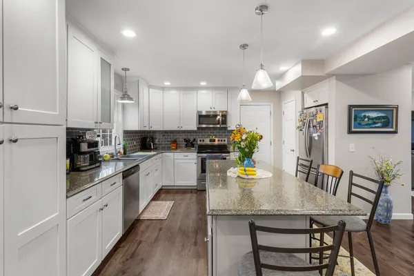 a kitchen with stainless steel appliances granite countertop a refrigerator a sink dishwasher a stove and white cabinets with wooden floor