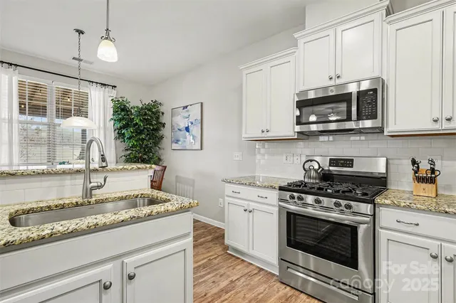 a kitchen with granite countertop a sink stainless steel appliances and white cabinets