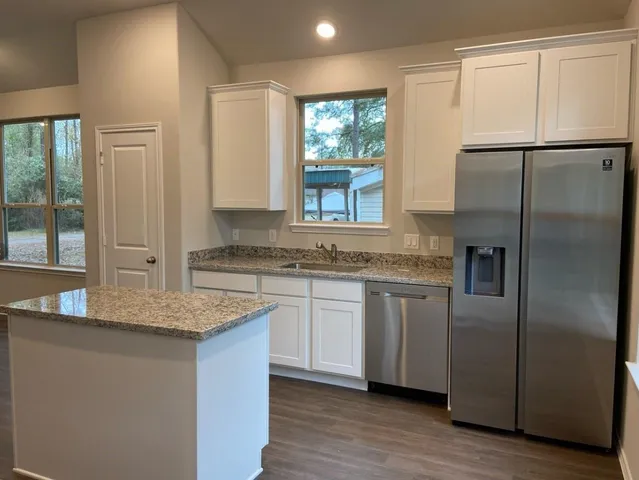 a kitchen with stainless steel appliances granite countertop a refrigerator a sink and white cabinets