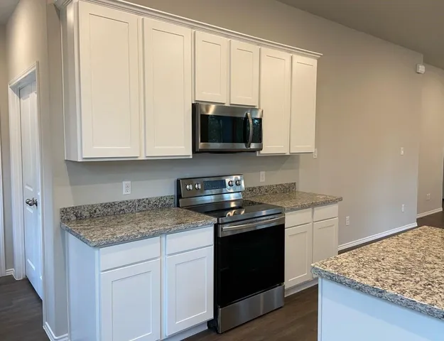 a kitchen with stainless steel appliances granite countertop white cabinets and a stove top oven