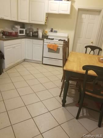 Kitchen with white cabinetry, white stove, dark countertops, and light tile patterned floors