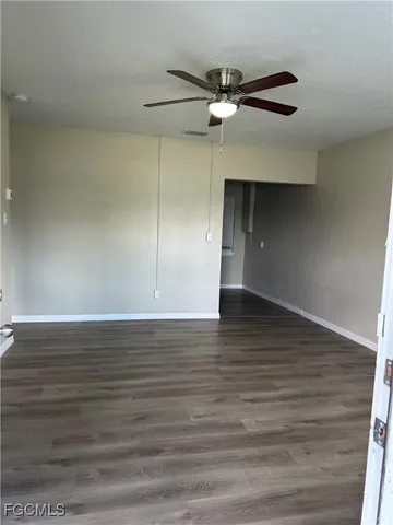a view of an empty room with wooden floor and a ceiling fan
