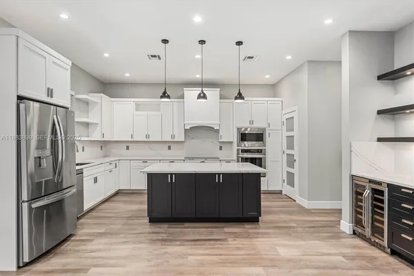 a large kitchen with stainless steel appliances kitchen island granite countertop a refrigerator and a stove top oven