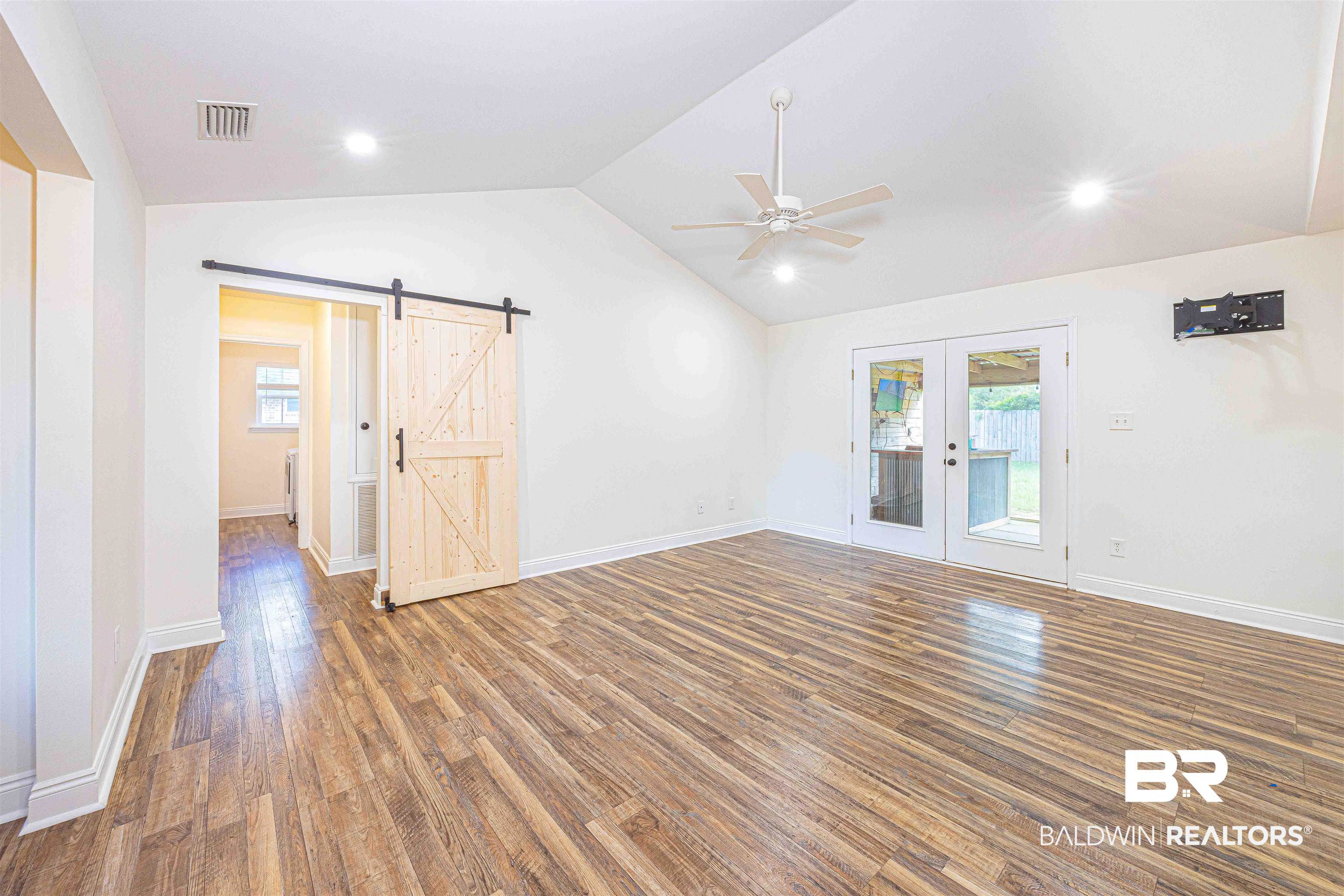 18675 Explorer Drive Loxley, AL 36551 - Photo 8 of 42 Empty room featuring french doors, ceiling fan, a barn door, wood finished floors, and vaulted ceiling