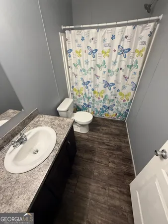 a bathroom with a granite countertop toilet a sink a mirror and shower curtain