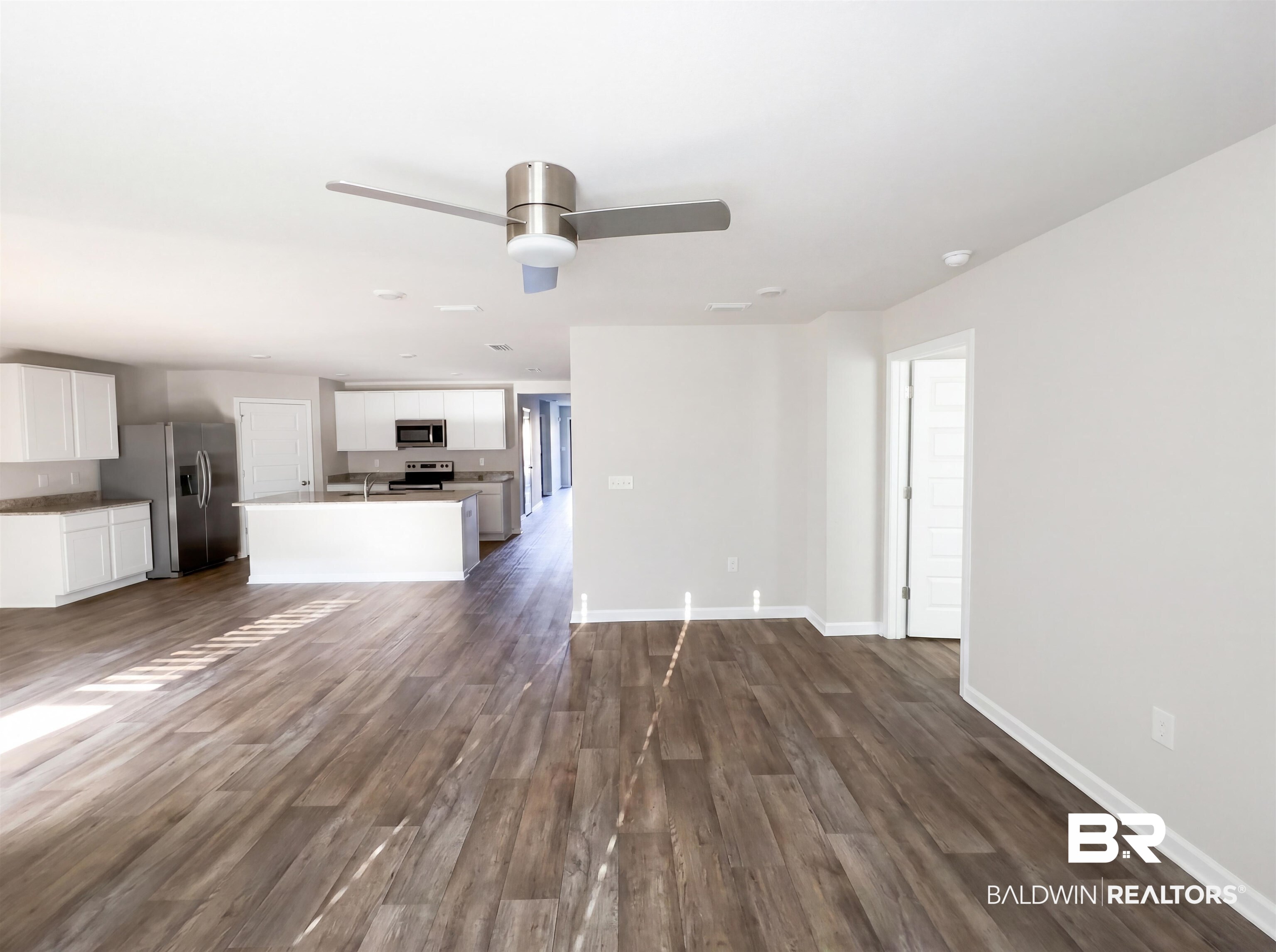 7453 Brompton Drive Foley, AL 36535 - Photo 3 of 15 Open-concept living area featuring wood-finish flooring, a modern ceiling fan, recessed lighting, white walls, and a visible kitchen with an island, white cabinetry, and stainless steel appliances