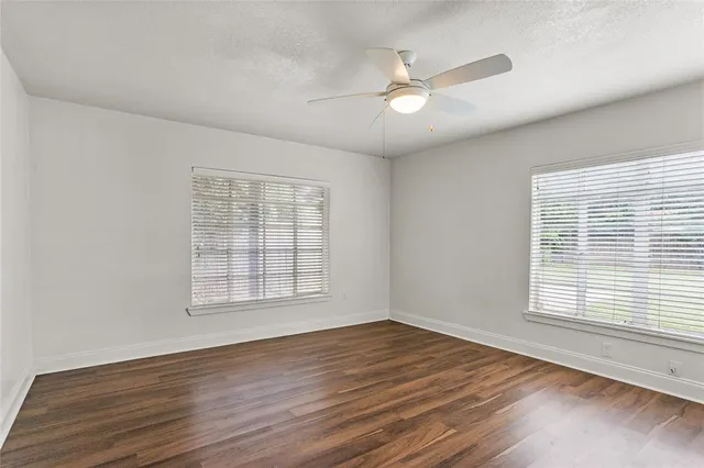 an empty room with wooden floor chandelier fan and windows